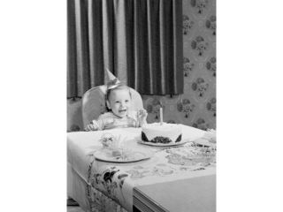 Baby girl wearing birthday hat sitting behind table with birthday cake Poster Print (18 x 24)